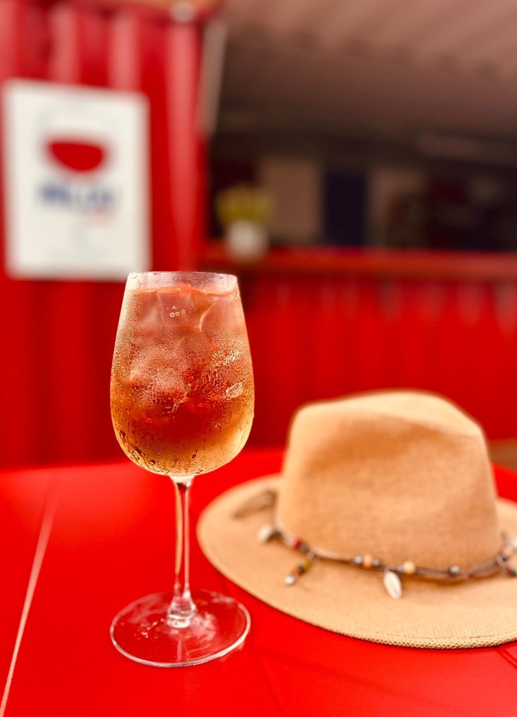 A spritz cocktail beside a hat on a red surface